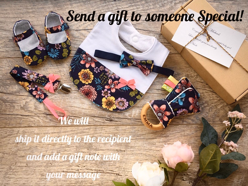 May include: A gift set for a baby, featuring a floral print bib, a bow tie, a pair of shoes, a teether, and a pacifier clip. The set is packaged in a brown box with a gift note.