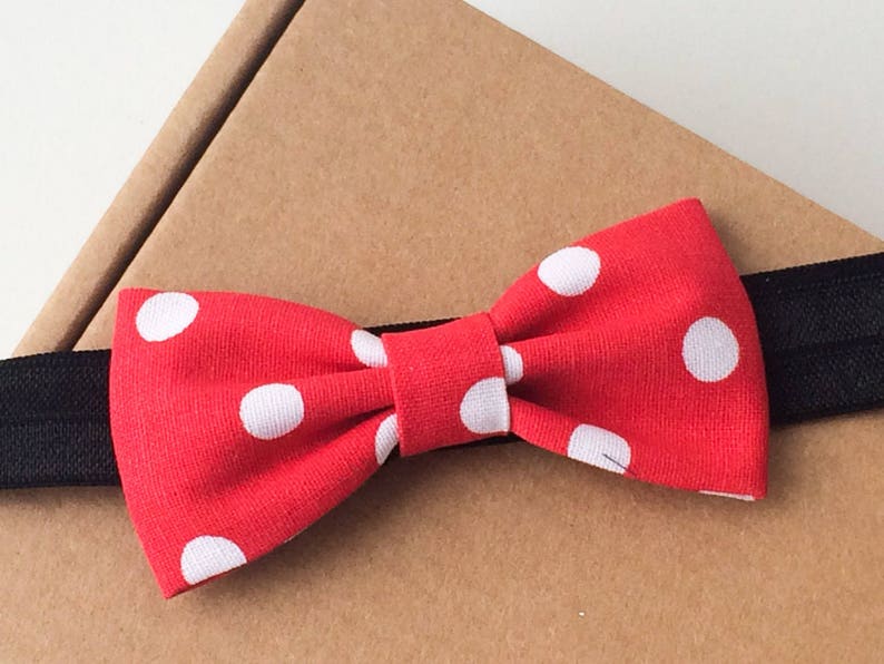 May include: Red bow tie with white polka dots on a black elastic headband.
