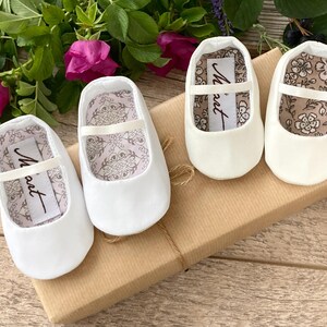 May include: Three pairs of white satin baby shoes with a satin ribbon and a small label that says "Maut" on each shoe.