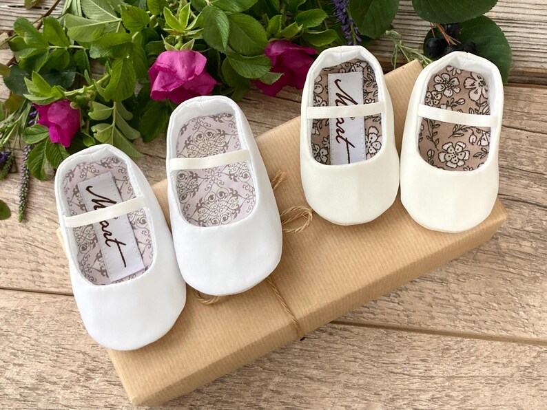 May include: Three pairs of white satin baby shoes with a satin ribbon and a small label that says "Maut" on each shoe.