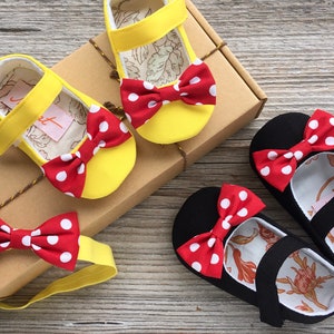 May include: A set of two pairs of baby shoes with red and white polka dot bows. One pair is yellow and the other is black. A matching red and white polka dot bow headband is included.