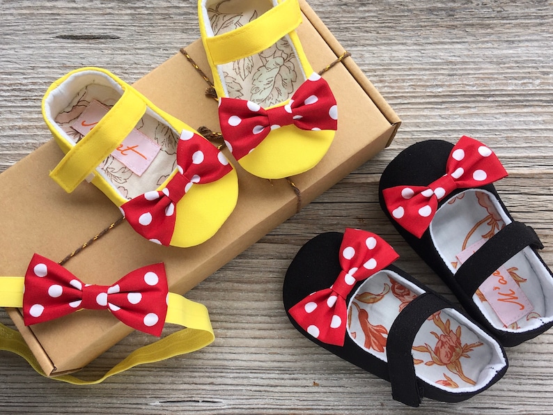 May include: A set of two pairs of baby shoes with red and white polka dot bows. One pair is yellow and the other is black. A matching red and white polka dot bow headband is included.