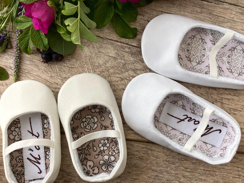 May include: Two pairs of white satin baby shoes with a floral pattern lining. One pair has the word "Matt" written on the lining.