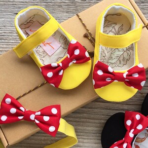 May include: Yellow baby shoes with red and white polka dot bows. The shoes are in a box with a matching headband.