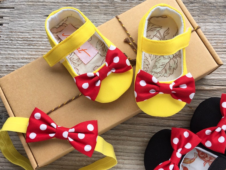 May include: Yellow baby shoes with red and white polka dot bows. The shoes are in a box with a matching headband.