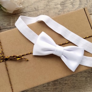 May include: A white bow tie with an elastic band, packaged in a brown box with twine and gold accents.
