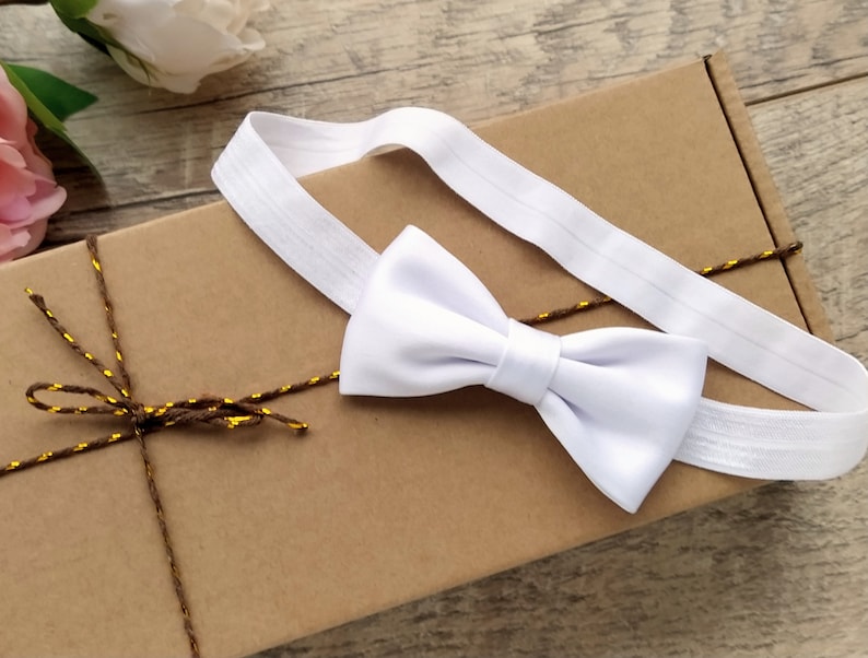 May include: A white bow tie with an elastic band, packaged in a brown box with twine and gold accents.