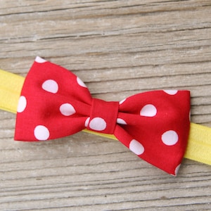 K&ouml;nnte beinhalten: Eine rote Schleife mit wei&szlig;en Punkten ist an einem gelben Haarreif befestigt.