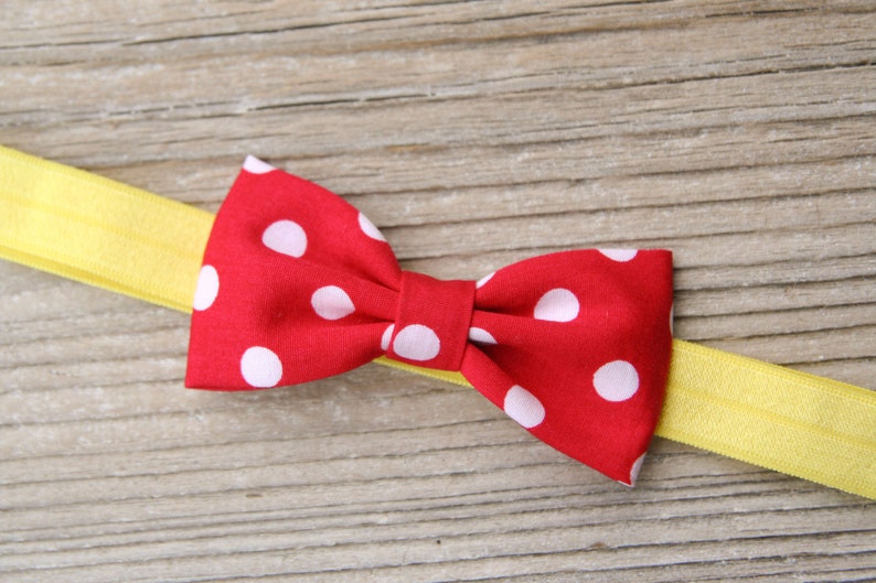 K&ouml;nnte beinhalten: Eine rote Schleife mit wei&szlig;en Punkten ist an einem gelben Haarreif befestigt.