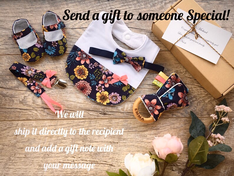May include: A baby gift set with a floral print. The set includes a bib, a bow tie, a pair of shoes, a teether, and a clip-on pacifier. The items are arranged on a wooden surface with the text "Send a gift to someone Special!" and "We will ship it directly to the recipient and add a gift note with your message."