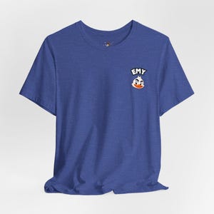 May include: A heather blue short-sleeve t-shirt featuring a small graphic on the left chest. The graphic depicts a cartoon duck head with an orange beak and the text EMY in white letters on a black background positioned above the duck head.