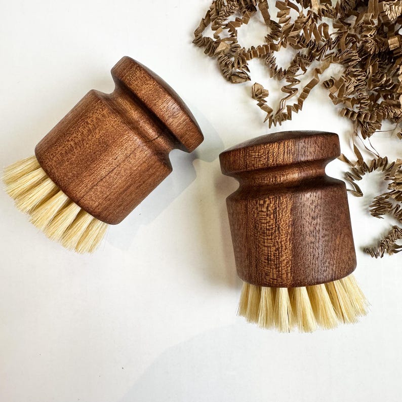 Puede incluir: Dos cepillos de madera para lavar platos con cerdas de color claro. Los cepillos tienen un dise&ntilde;o redondeado y ergon&oacute;mico y est&aacute;n hechos de madera marr&oacute;n oscura. Las cerdas est&aacute;n muy juntas y parecen estar hechas de fibras naturales. El fondo es blanco con papel marr&oacute;n.