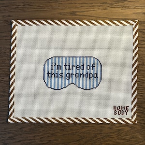 May include: A white canvas with a brown and white striped border. The canvas features a blue sleep mask design with the text "I'm tired of this grandpa." The lower right corner has the text "HOME BODY."