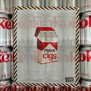 Puede incluir: Obra de arte de punto de cruz que representa un paquete de cigarrillos rojo y blanco con el texto "FRIDGE cigs". La obra está enmarcada con un borde a rayas marrón y blanco. Las palabras "HOME BODY" están en la parte inferior. Latas de Coca-Cola Light en el fondo.