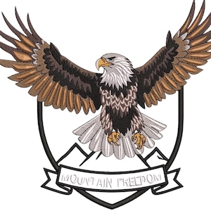 May include: Embroidered image of an eagle with spread wings, in brown, black, and white. The eagle is set against a shield, with the text "MOUNTAIN FREEDOM" on a banner below, depicting a mountain range.