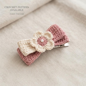 Può includere: Una molletta per capelli all'uncinetto con un fiocco rosa polvere e crema, decorata con un fiore centrale color crema e una piccola perla bianca. Il testo CROCHET PATTERN AVAILABLE Instant Download è visibile sopra l'accessorio.