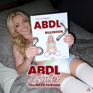 May include: A white booklet titled The Ultimate ABDL Beginners Rulebook featuring a graphic illustration of a character with pink hair wearing a white top and diaper. The cover includes metallic silver accents and the text ABDL Rules You NEED to Know.