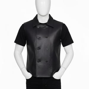 May include: A black leather vest with a double-breasted design, featuring six dark buttons and a collared neckline. The vest is worn over a black t-shirt and paired with black jeans. The mannequin's hands are in the pockets.