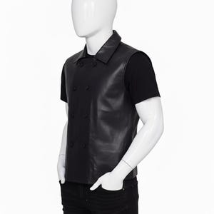 May include: A black leather vest with a double-breasted button closure. The vest has a collared neckline and is worn over a black t-shirt and black jeans. The mannequin is set against a white background.