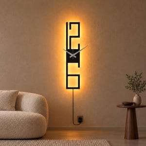 May include: A vertical black wall clock with a rectangular frame featuring the numbers 12 and 6 in a stylized font. The clock has thin silver hands and is illuminated from behind by a warm, glowing light, with a black power cord extending downward.