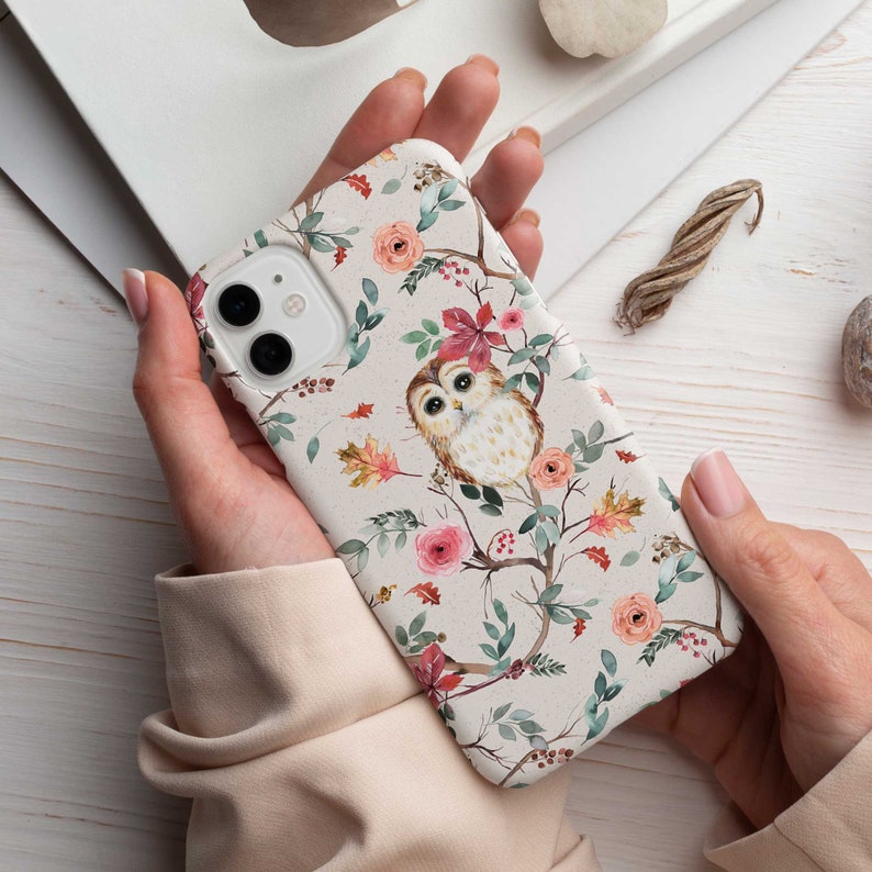 Puede incluir: Una funda de tel&eacute;fono blanca con un dise&ntilde;o de acuarela de un b&uacute;ho posado en una rama con flores rosas y rojas y hojas verdes.