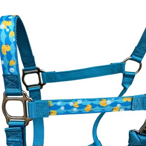 Pu&ograve; includere: Un cavezza blu per cavalli con un motivo di anatre di gomma gialle. La cavezza ha ferramenta argentata e una chiusura a scatto.