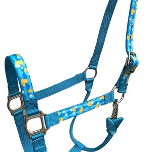 Pu&ograve; includere: Un cavezza blu per cavalli con un motivo di anatre di gomma gialle. La cavezza ha una fibbia argentata e un anello argentato sul naso. La cavezza &egrave; realizzata in nylon ed &egrave; regolabile.