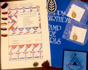 May include: A collection of Camp Fire Girls memorabilia, including a Group Charter, a blue "Happy Birthday Camp Fire Girls" card, and various pins and patches. The charter features red, white, and blue geometric designs.