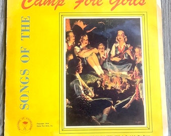 Könnte beinhalten: Vintage Albumcover mit dem Titel "Songs of the Camp Fire Girls" mit gelbem Hintergrund. Das Cover zeigt ein Gemälde einer Gruppe von Mädchen am Lagerfeuer. Der Text enthält "Camp Fire Girls" und "Records of Knowledge".