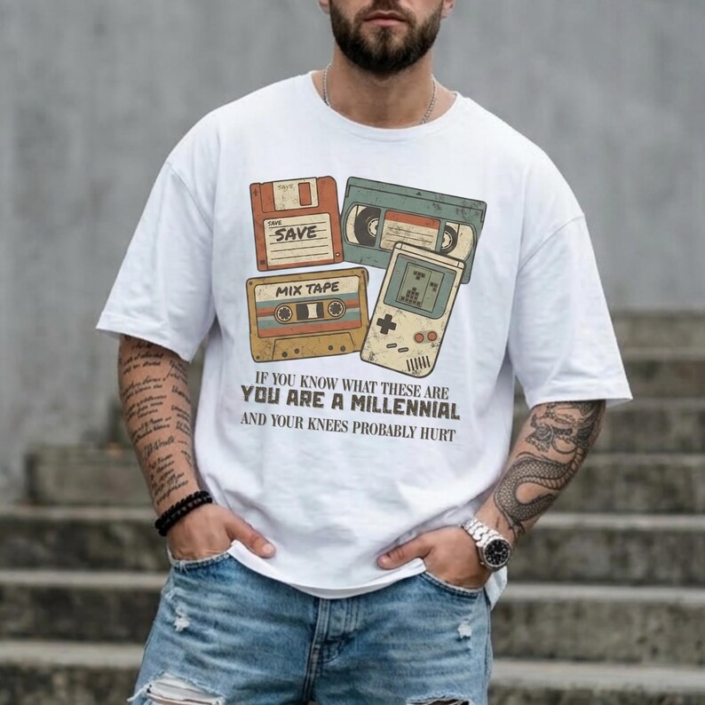 May include: White t-shirt featuring retro graphics of a floppy disk, VHS tape, cassette tape, and handheld game console. The shirt includes the text: "IF YOU KNOW WHAT THESE ARE YOU ARE A MILLENNIAL AND YOUR KNEES PROBABLY HURT."