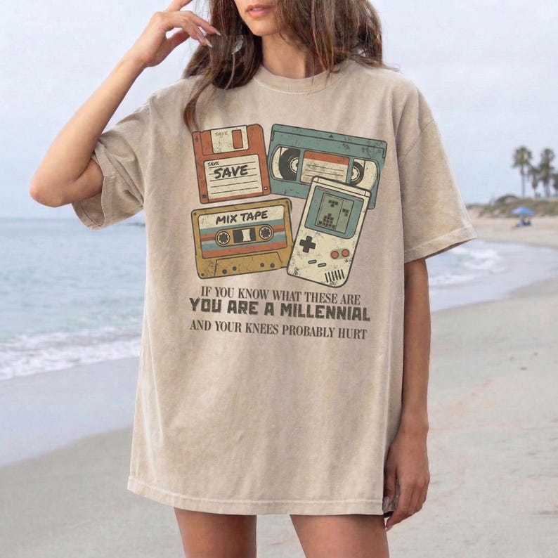 Retro-style graphic design featuring 90s nostalgia icons: a floppy disk, a VHS tape, a cassette "Mix Tape," and a handheld gaming console. The illustrations have a distressed, vintage aesthetic in muted tones of orange, teal, and yellow. Below the graphics, bold text reads: "IF YOU KNOW WHAT THESE ARE YOU ARE A MILLENNIAL AND YOUR KNEES PROBABLY HURT." The overall vibe is humorous and nostalgic, perfect for millennial humor and pop culture fans.