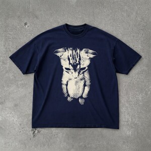 Peut inclure: Un t-shirt bleu marine &agrave; manches courtes avec une impression graphique blanc cass&eacute; centr&eacute;e repr&eacute;sentant un chaton. L'illustration du chaton pr&eacute;sente un motif textur&eacute; en demi-teintes et est vue d'un angle &eacute;lev&eacute;, la t&ecirc;te inclin&eacute;e vers le bas.