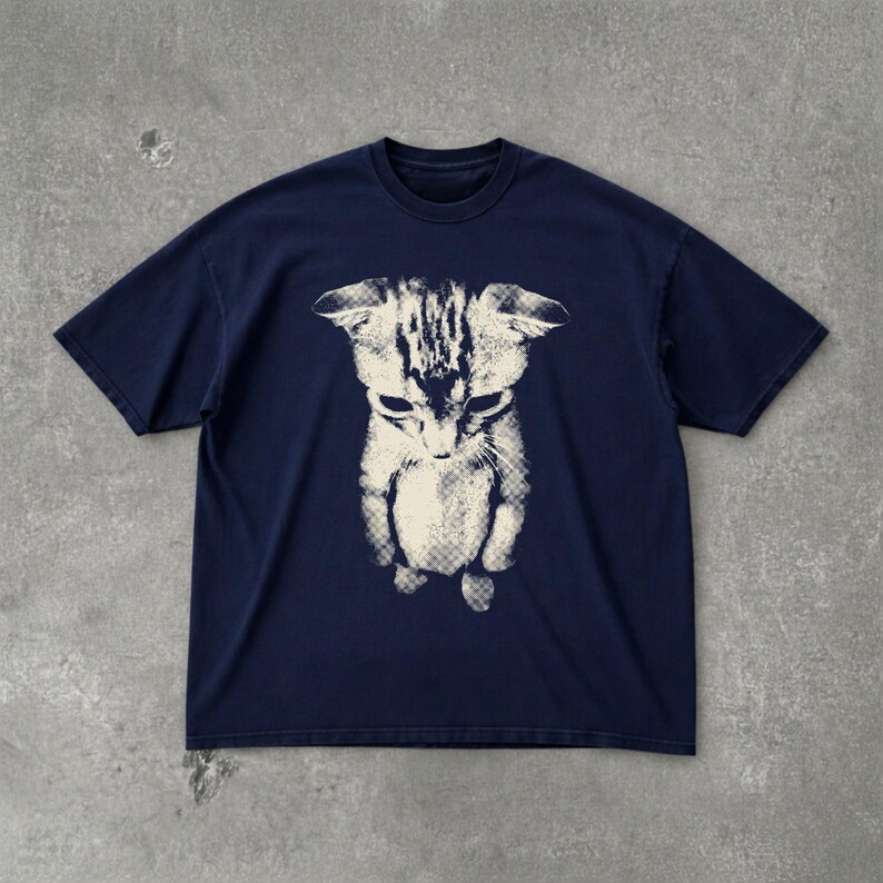 Peut inclure: Un t-shirt bleu marine &agrave; manches courtes avec une impression graphique blanc cass&eacute; centr&eacute;e repr&eacute;sentant un chaton. L'illustration du chaton pr&eacute;sente un motif textur&eacute; en demi-teintes et est vue d'un angle &eacute;lev&eacute;, la t&ecirc;te inclin&eacute;e vers le bas.