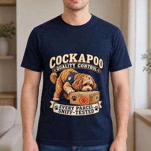 May include: A navy blue short-sleeve t-shirt featuring a graphic of a golden-brown Cockapoo dog wearing a blue harness. The dog is sniffing a cardboard box. Text reads: COCKAPOO QUALITY CONTROL EVERY PARCEL SNIFF-TESTED with paw print accents.