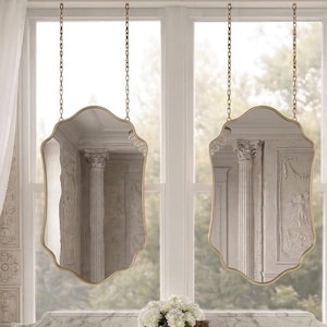 Puede incluir: Dos espejos decorativos colgantes con marcos dorados y bordes ondulados. Los espejos están suspendidos por cadenas frente a una ventana. Los espejos reflejan un interior arquitectónico clásico con una columna.