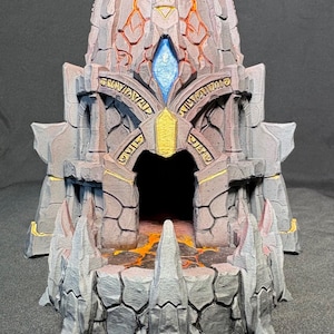May include: A detailed, gray and gold fantasy structure with a central archway, a blue gem, and intricate detailing. The design includes sharp, stone-like elements and a fiery orange interior, suggesting a dungeon or temple.