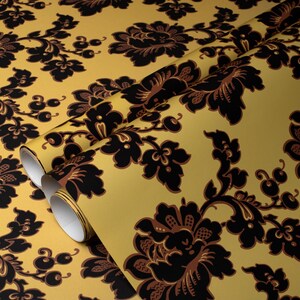 May include: A roll of wallpaper with a repeating floral pattern. The design features large, stylized black flowers and foliage against a golden-yellow background. The wallpaper is rolled up, revealing the white backing.
