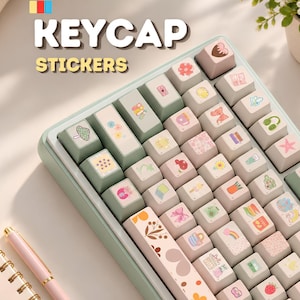 Puede incluir: Un teclado mecánico con teclas de color verde claro y rosa pálido decoradas con varias pegatinas gráficas pequeñas y coloridas. El texto KEYCAP STICKERS aparece en la esquina superior izquierda. El teclado tiene un marco verde claro.