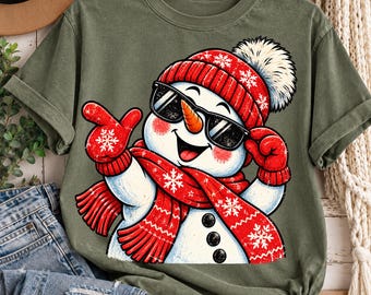 May include: An olive green t-shirt featuring a graphic of a smiling snowman wearing black sunglasses, a red knit hat with a white pom-pom, and a matching red scarf with white snowflake patterns. The snowman has a carrot nose and red mittens.