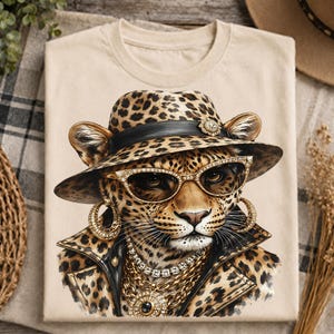 May include: A beige t-shirt featuring a graphic print of a leopard wearing a leopard-print fedora with a black band, gold-rimmed sunglasses, large gold hoop earrings, a layered gold chain necklace with a pendant, and a leopard-print leather jacket.