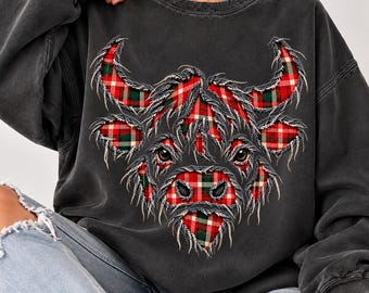 May include: A charcoal gray crewneck sweatshirt featuring a central graphic of a Highland cow head. The cow is filled with a red, green, and white plaid pattern and has a distressed, frayed-edge appearance around the horns and face.