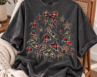 May include: A charcoal gray short-sleeve t-shirt featuring a graphic of a Christmas tree constructed from distressed, frayed fabric patches in red and green plaid, leopard print, and camouflage patterns, topped with a plaid bow.