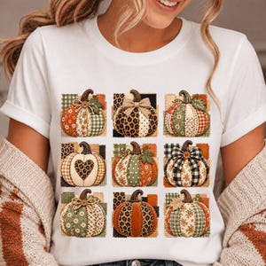 Puede incluir: Una camiseta blanca de manga corta con un estampado gráfico de nueve calabazas dispuestas en cuadrícula. Cada calabaza muestra un diseño de patchwork único con varios patrones que incluyen leopardo, cuadros, flores y lunares en tonos otoñales.