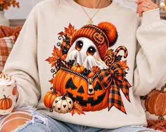 May include: A beige crewneck sweatshirt featuring a graphic of a white ghost wearing an orange knit hat with a pumpkin design. The ghost sits inside a large orange jack-o'-lantern with a zipper, surrounded by autumn leaves and a plaid bow.