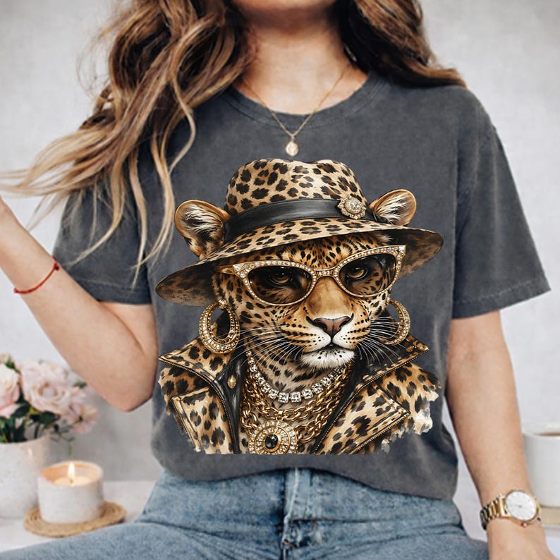 May include: A charcoal gray t-shirt featuring a graphic print of a leopard wearing a leopard-print fedora, gold-rimmed sunglasses, large gold hoop earrings, a layered gold chain necklace, and a black leather-style jacket with gold accents.