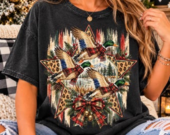 May include: A charcoal gray short-sleeve t-shirt featuring a graphic of three mallard ducks wearing plaid scarves. The design includes a large star, leopard print accents, pine branches, red berries, and a plaid bow with two gold bells.