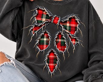 May include: A charcoal gray crewneck sweatshirt featuring a large, distressed-style graphic of a bow and three hanging ornaments. The graphic has a red, green, and white plaid pattern with frayed, raw-edge detailing around the shapes.