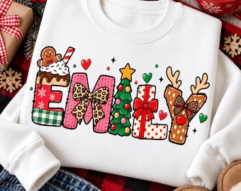 May include: A white long-sleeve sweatshirt featuring the name EMILY in large, decorative letters. The letters are styled with Christmas themes including a gingerbread man, a leopard print bow, a green pine tree, a gift box, and reindeer antlers.