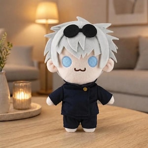 Könnte beinhalten: Plüschpuppe einer Figur mit weißem Haar, schwarzer Sonnenbrille und blauen Augen. Die Puppe trägt eine dunkelblaue Uniform mit einem goldenen Knopf. Die Puppe steht auf einem Holztisch.