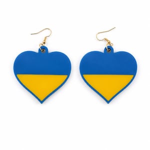 May include: A pair of heart-shaped earrings featuring a horizontal bicolour design of blue on the top half and yellow on the bottom half. Each earring is suspended from a gold-toned metal hook, creating a symmetrical set of dangling jewellery.